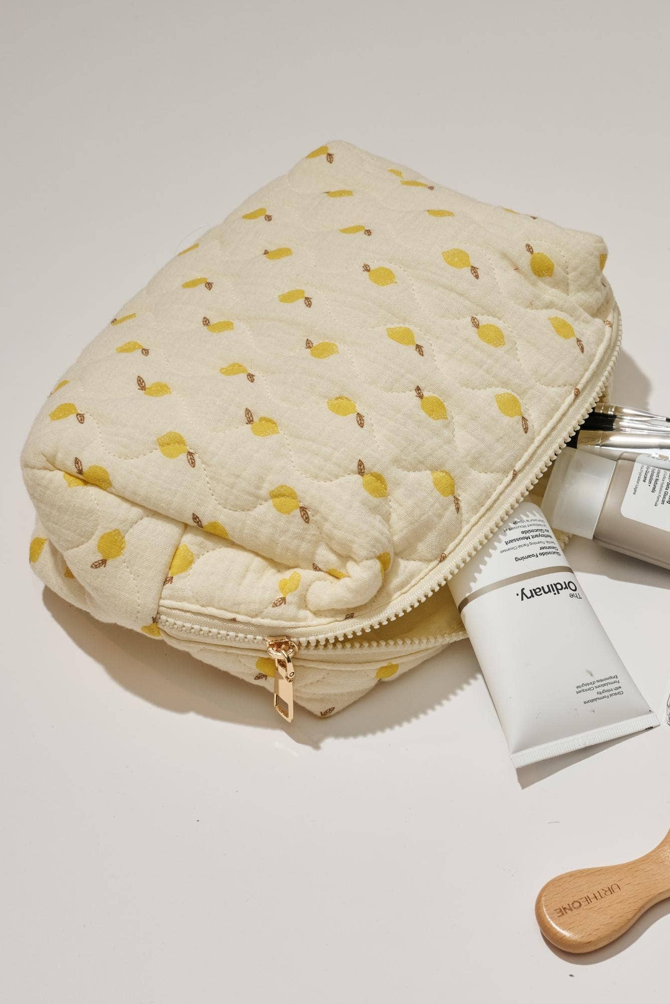 Cosmetic bag with toiletries including a brush and bottles on a light background