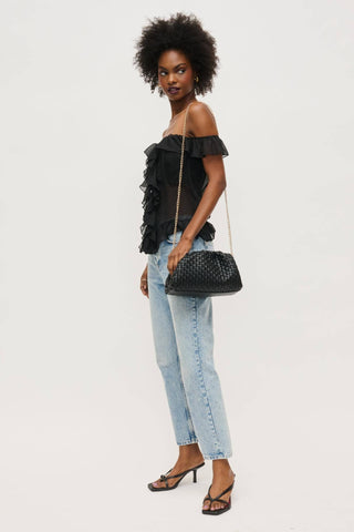 Woman wearing a black off-shoulder top and light blue jeans, holding a black handbag on a white background