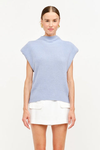 Woman wearing a light blue sleeveless top and white shorts on a white background