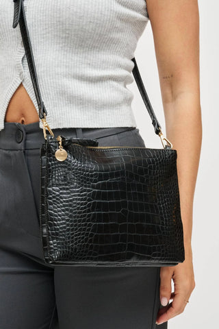 Woman wearing black croc texture crossbody bag with gold hardware and adjustable strap