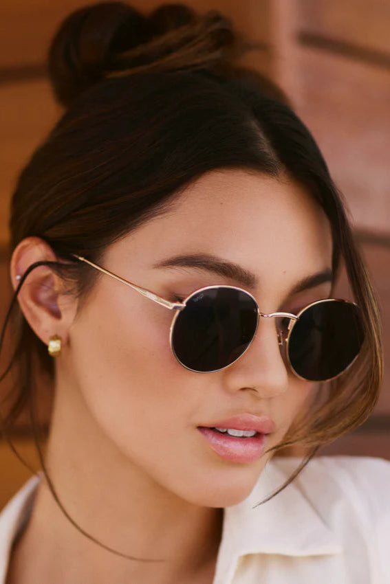 Woman wearing round sunglasses with a blurred wooden background
