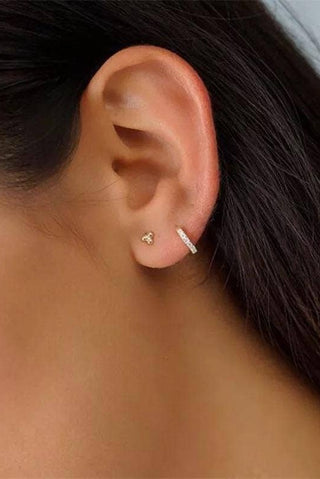Woman wearing delicate silver pavé huggie earrings styled in a second piercing stack