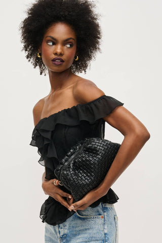 Woman wearing a black off-shoulder top and holding a black textured bag against a light gray background