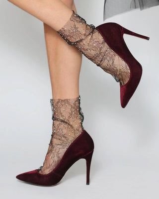 Maroon high-heeled shoes with lace detailing worn by a person on a light gray background