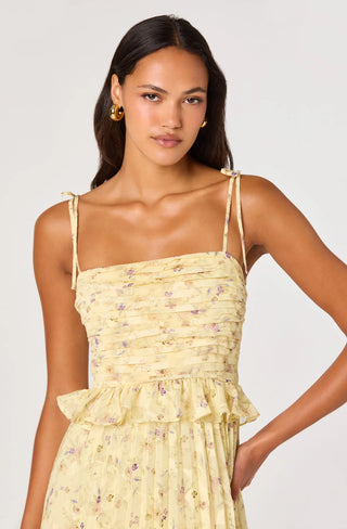 Woman wearing a yellow floral dress against a plain background
