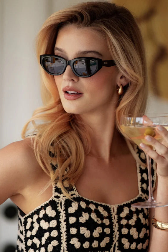 Woman holding a glass of orange juice with sunglasses on, wearing a black and white patterned dress.