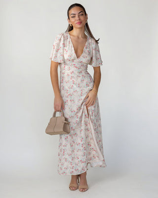 Woman wearing a floral dress holding a handbag against a white background