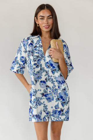Front detail of women's Cala floral cotton denim mini dress showing wide notched collar, deep V neckline and sky to navy blue floral print on white