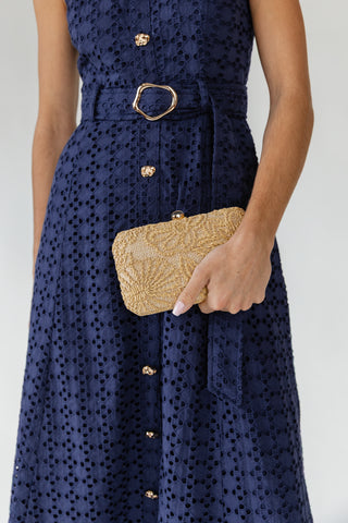 Navy dress with gold buttons and a hand holding a gold clutch against a white background