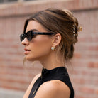 Woman wearing sunglasses and a black sleeveless top against a brick wall.