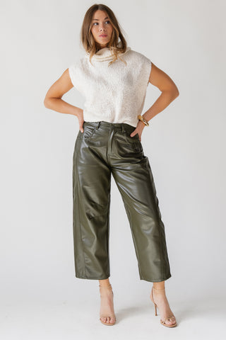 Woman wearing a white sweater and green leather pants on a plain background