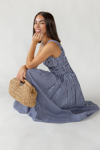 Woman in a blue checkered dress holding a woven handbag against a white background