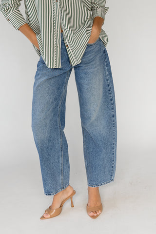 A person wearing wide-leg blue denim jeans with a striped button-up shirt and tan heeled sandals, shown from the waist down against a plain light background.