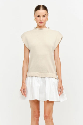 Woman wearing a beige sleeveless top and white skirt on a white background