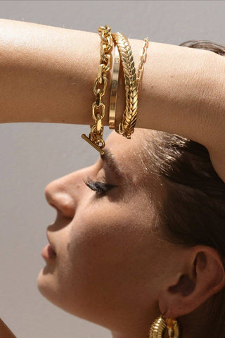 Woman wearing gold jewelry including earrings, bracelets, and necklaces against a neutral background