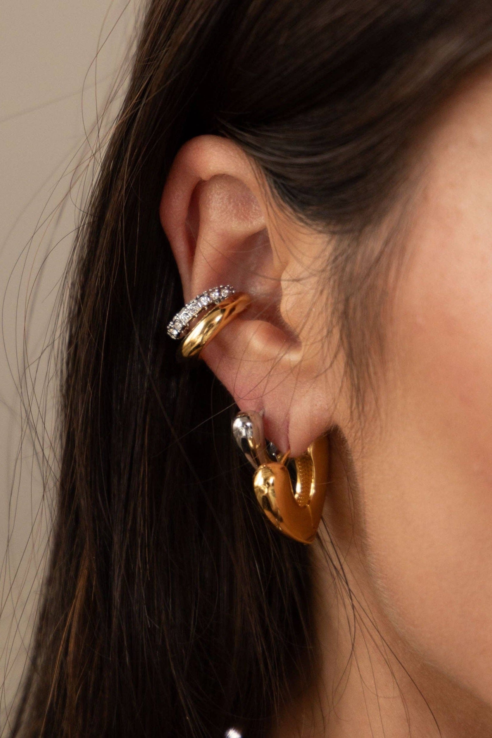 Close-up of an ear wearing gold hoop earrings with a neutral background