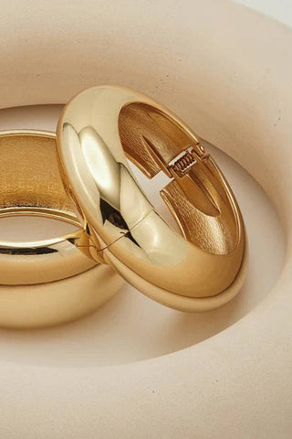 Two gold bangle bracelets on a beige surface