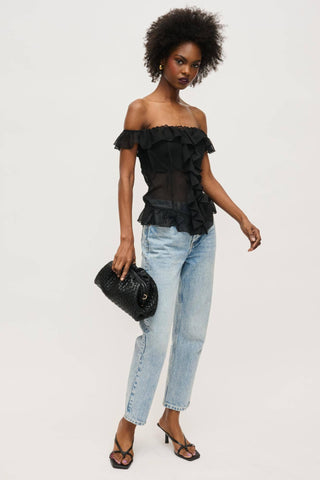 Woman wearing a black ruffled top and light blue jeans on a white background