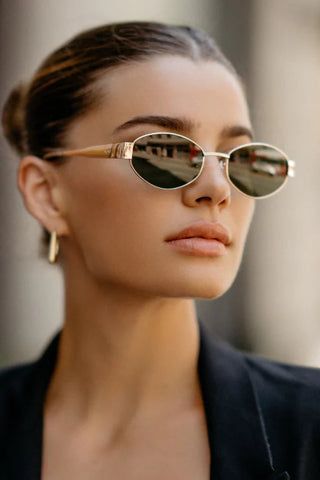 Woman wearing gold-framed sunglasses with a blurred background